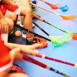 Children playing floorball. Boys holding floor ball sticks resting on the bench during a match