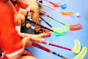 Children playing floorball. Boys holding floor ball sticks resting on the bench during a match
